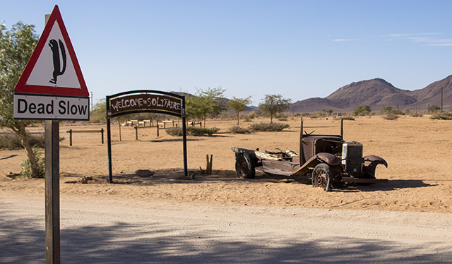 Lugar solitario y pintoresco en mitad de la nada en Namibia. Esqueleto oxidado de coche muy antiguo, cartel de welcome to Solitaire, y señal de peligro de perritos de las praderas que insta a conducir despacio para no atropellarlos.  