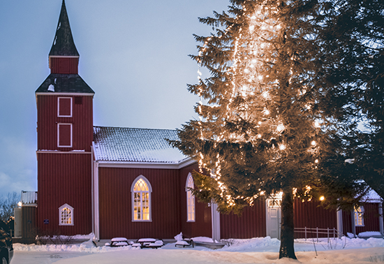 Iglesia roja, con algo de nieve en el techo, en primer plano un abeto natural decorado y encendido