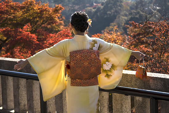 chica con kimono amaraillo y fondo de copas de árboles en otoño